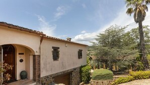 Un edificio tradicional con fachada de piedra, techo de tejas y un pequeño jardín con una palmera y arbustos.