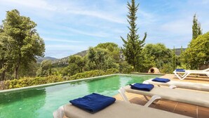 Una piscina infinita con sillas de descanso y toallas, rodeada de exuberante vegetación y colinas al fondo.