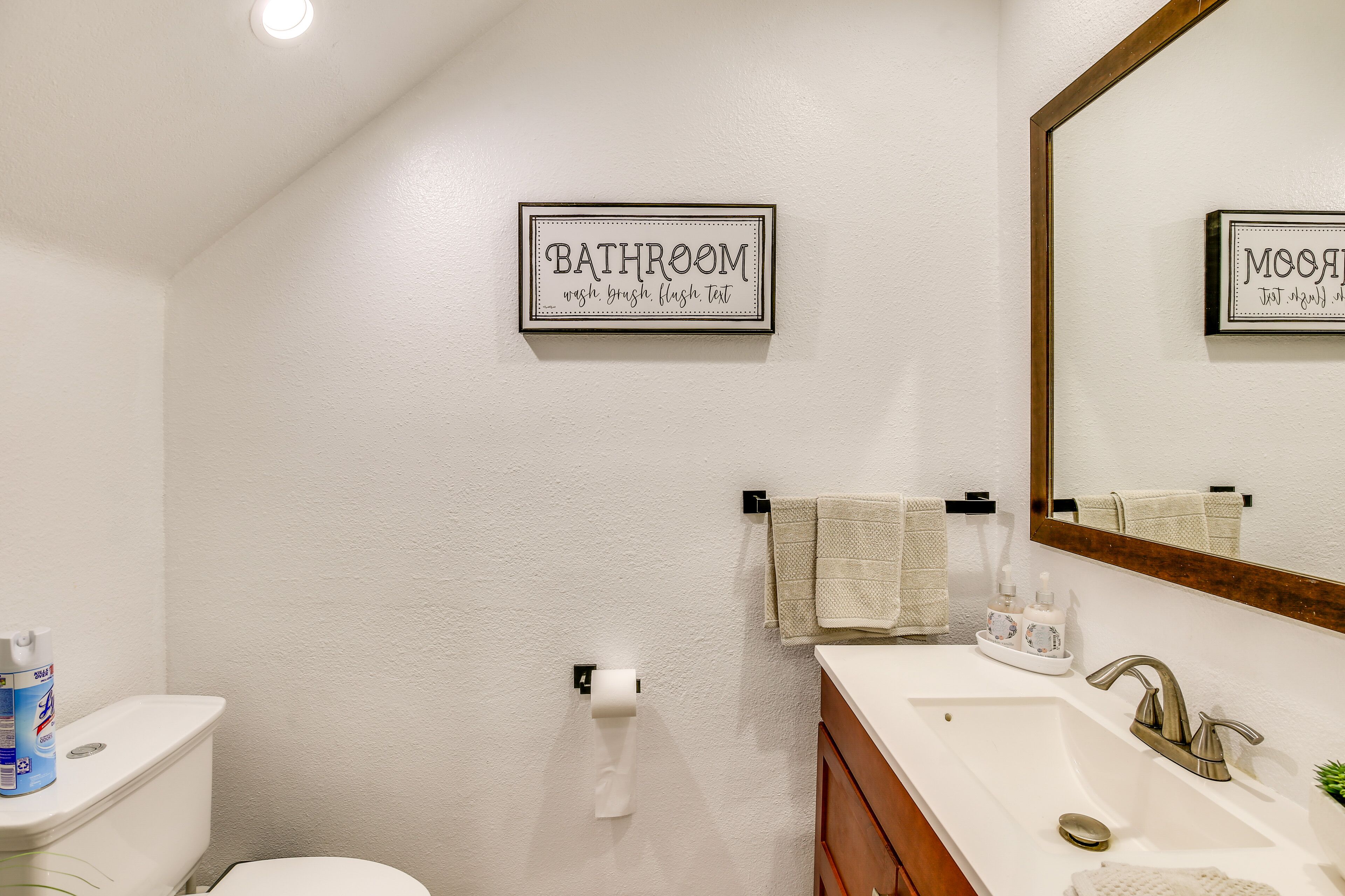 A bathroom with a toilet, sink, and mirror. There is a sign on the wall that reads "BATHROOM wash brush flush text."
