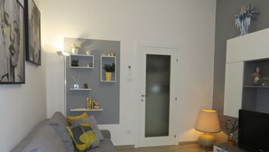 A modern living room with a grey sofa, a flat-screen TV, and a door with frosted glass panels. - Beautiful apartment for 4 guests with WIFI, A/C, TV and balcony (Bologna)