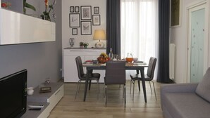 A modern living room with a grey sofa, a dining area with a table and chairs, and a kitchen area with a fridge and a TV. - Beautiful apartment for 4 guests with WIFI, A/C, TV and balcony (Bologna)
