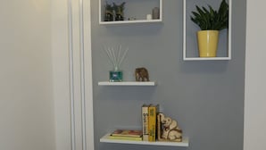 A living room with a grey sofa, a floor lamp, and three white shelves with various decorative items. - Beautiful apartment for 4 guests with WIFI, A/C, TV and balcony (Bologna)