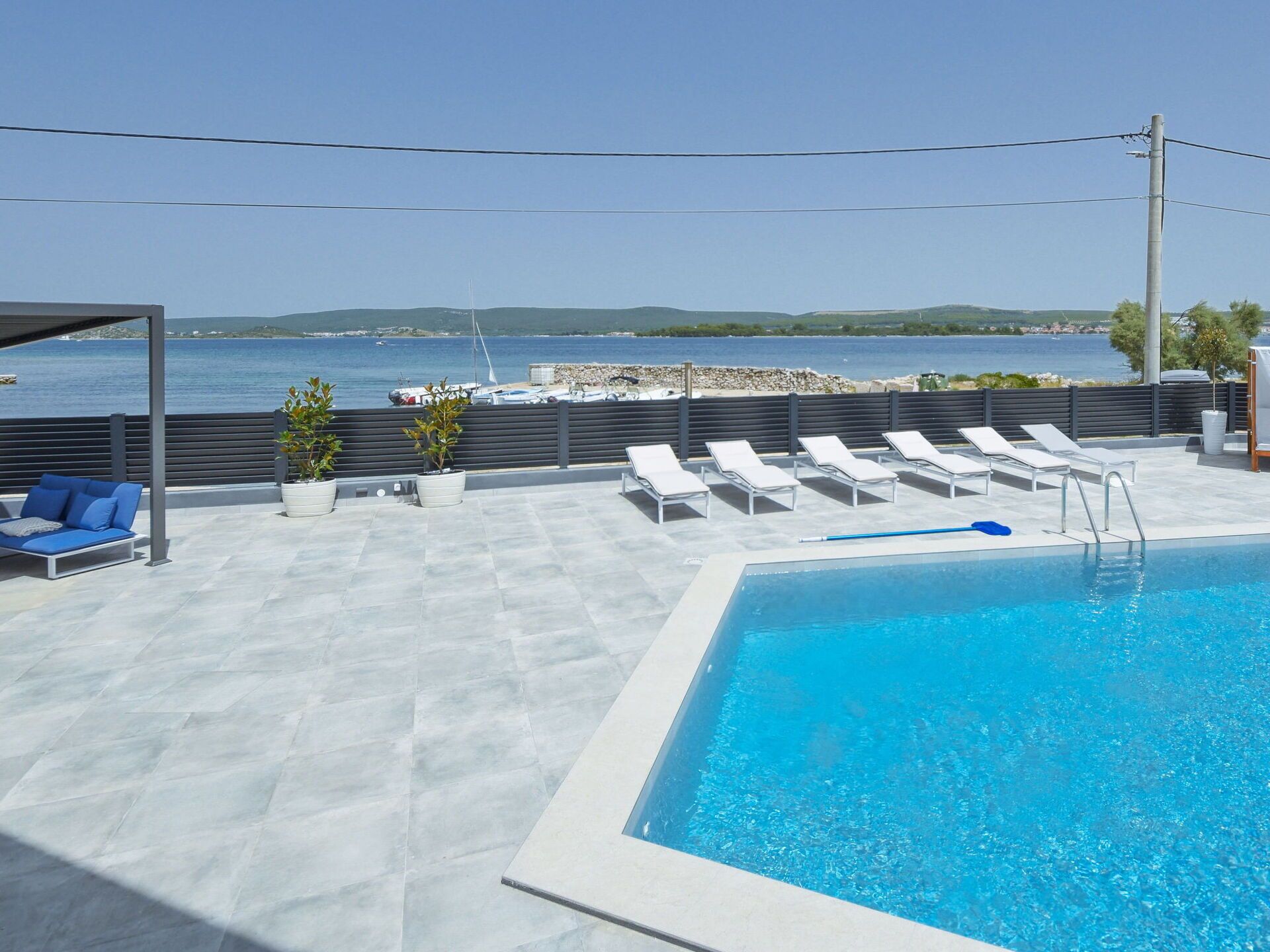 Ein Pool auf dem Dach mit Liegestühlen und einer Sitzgelegenheit, mit Blick auf ein Gewässer und das ferne Land.
