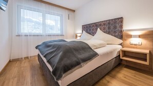 Une chambre à coucher moderne avec un grand lit, une table de chevet avec une lampe et une fenêtre ornée de rideaux légers.