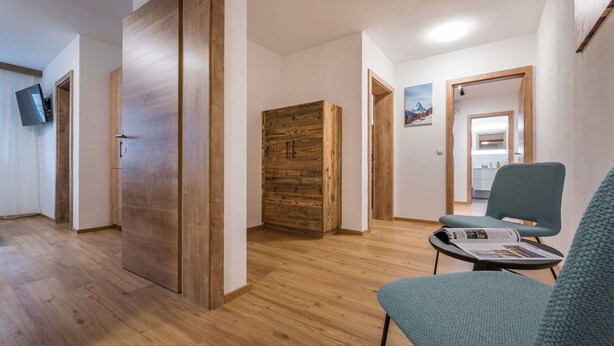 Un intérieur moderne avec un plancher en bois, un fauteuil recouvert d’un tissu vert, une armoire en bois et un téléviseur à écran plat fixé au mur.