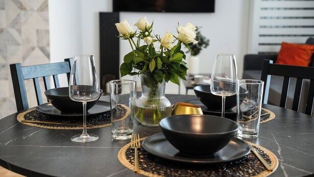A dining table set with black bowls, wine glasses, and a vase with white flowers. - Maria (Bucharest)