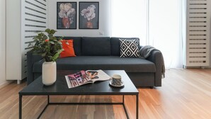 A modern living room with a grey sofa, a black coffee table, a white vase with green plants, and two framed floral artworks on the wall. - Maria (Bucharest)