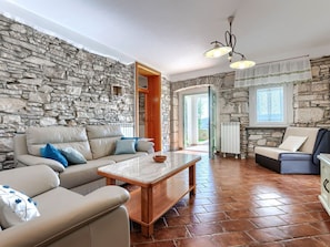 Uma sala de estar com paredes de pedra, lareira de pedra, mesa de centro de madeira e piso de pedra.