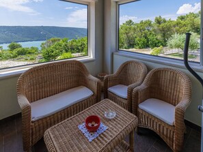 A balcony with wicker furniture, a small table, and a view of a lake and hills.