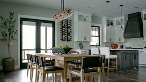 A modern kitchen with white cabinets, a wooden dining table, and a large window. - Located on Bear Lake in Tuckasegee, NC.  A scenic getaway for your family event! (Tuckasegee)