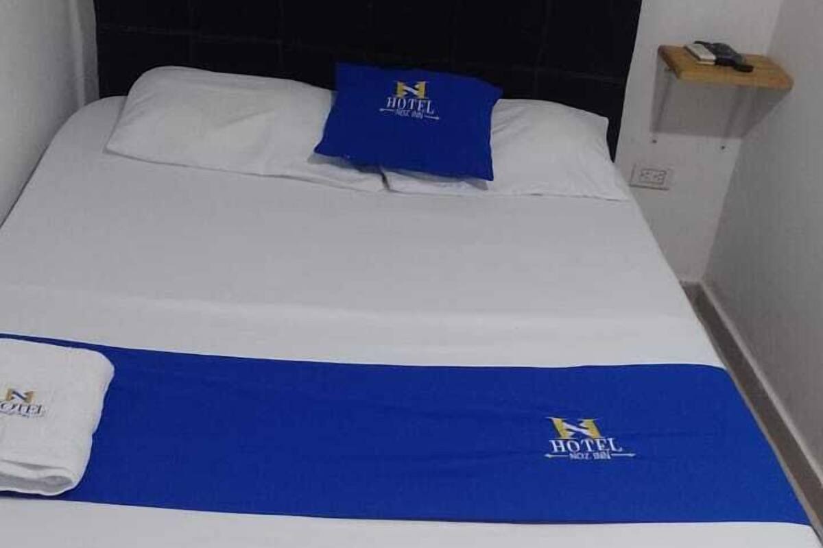 A hotel room with a bed, a blue blanket, and a pillow with the hotel logo.