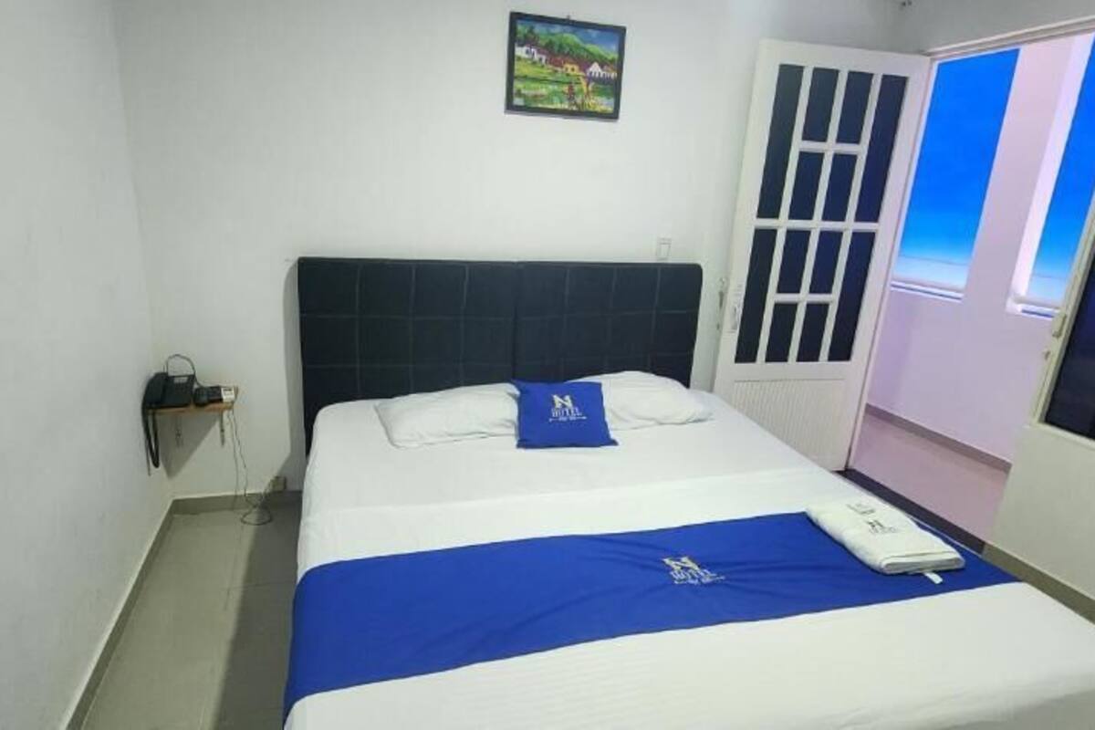 A hotel room with a bed, a nightstand, a window with a view, and a door with a screen.