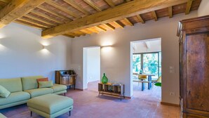 Un salon spacieux avec un plafond en bois, un canapé vert, un meuble en bois et un coin repas visible à travers une porte ouverte.
