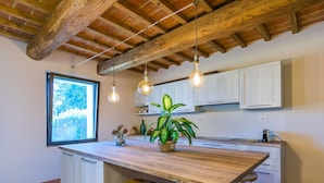 Une cuisine dotée d’un îlot central en bois, de tabourets de bar, de luminaires suspendus et d’une grande fenêtre.
