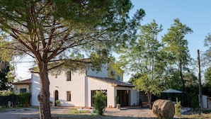 Une maison moderne avec un grand arbre au premier plan, un espace patio et une botte de foin.