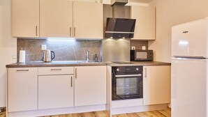 Una cocina moderna con armarios blancos, horno empotrado, microondas y una campana extractora de acero inoxidable.