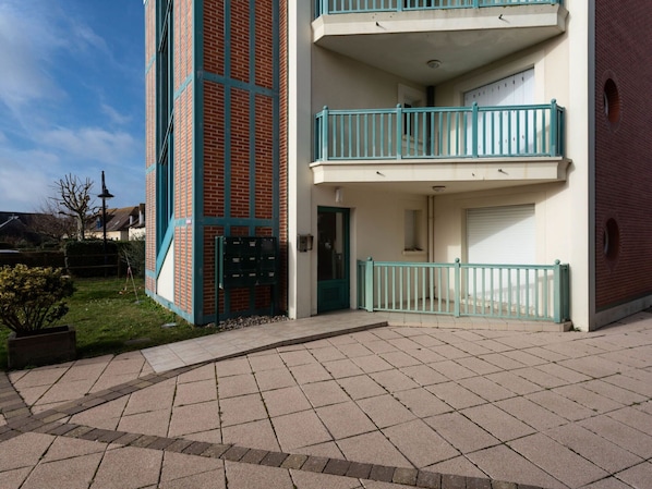 Stunning multi-story building with a brick facade and a flat roof, featuring a paved entrance area and a small garden.