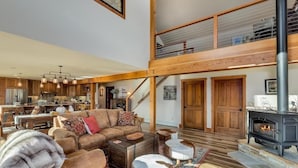 A spacious living area with a high ceiling, a fireplace, and a kitchen in the background.