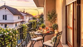 Un balcone con un tavolo apparecchiato per due, circondato da piante in vaso e vista sul tramonto.