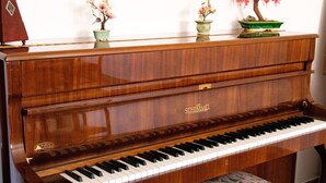 Un piano de cua amb acabat de fusta, col·locat davant d'una paret blanca.