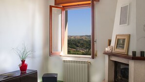 Habitació amb finestra gran, radiador, llar de foc, sofà i armari.