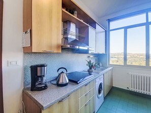 Een moderne keuken met een koffiezetapparaat, waterkoker en wasmachine, een raam met uitzicht en houten kastjes.