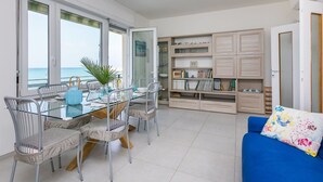 A modern living room with a glass dining table, metal chairs, a blue sofa, and a bookshelf. - Lovely apartment for 6 people with A/C, WIFI, TV and balcony (Rosignano Solvay-castiglioncello)