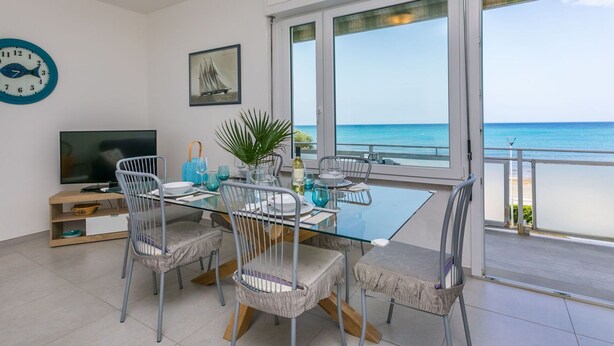 A modern dining area with a glass table, metal chairs, and a view of the sea. - Lovely apartment for 6 people with A/C, WIFI, TV and balcony (Rosignano Solvay-castiglioncello)