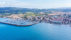 An aerial view of a coastal city with a marina, residential buildings, and hills in the background. - Lovely apartment for 6 people with A/C, WIFI, TV and balcony (Rosignano Solvay-castiglioncello)