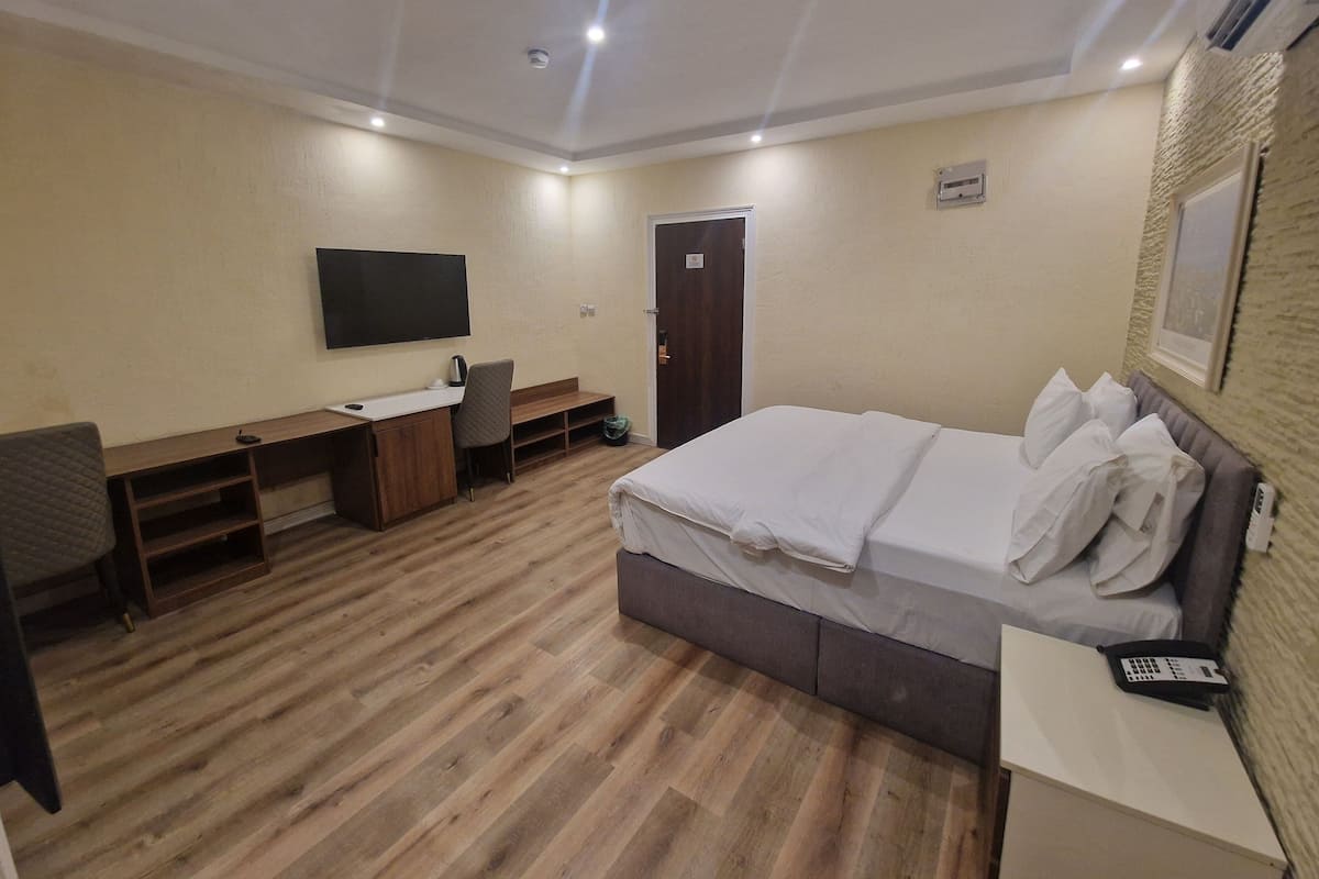 A hotel room with a bed, a desk, a chair, a TV, and a door.