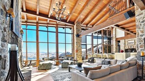 Un salón amplio con un sofá grande, vigas de madera, paredes de piedra y vistas a las montañas.