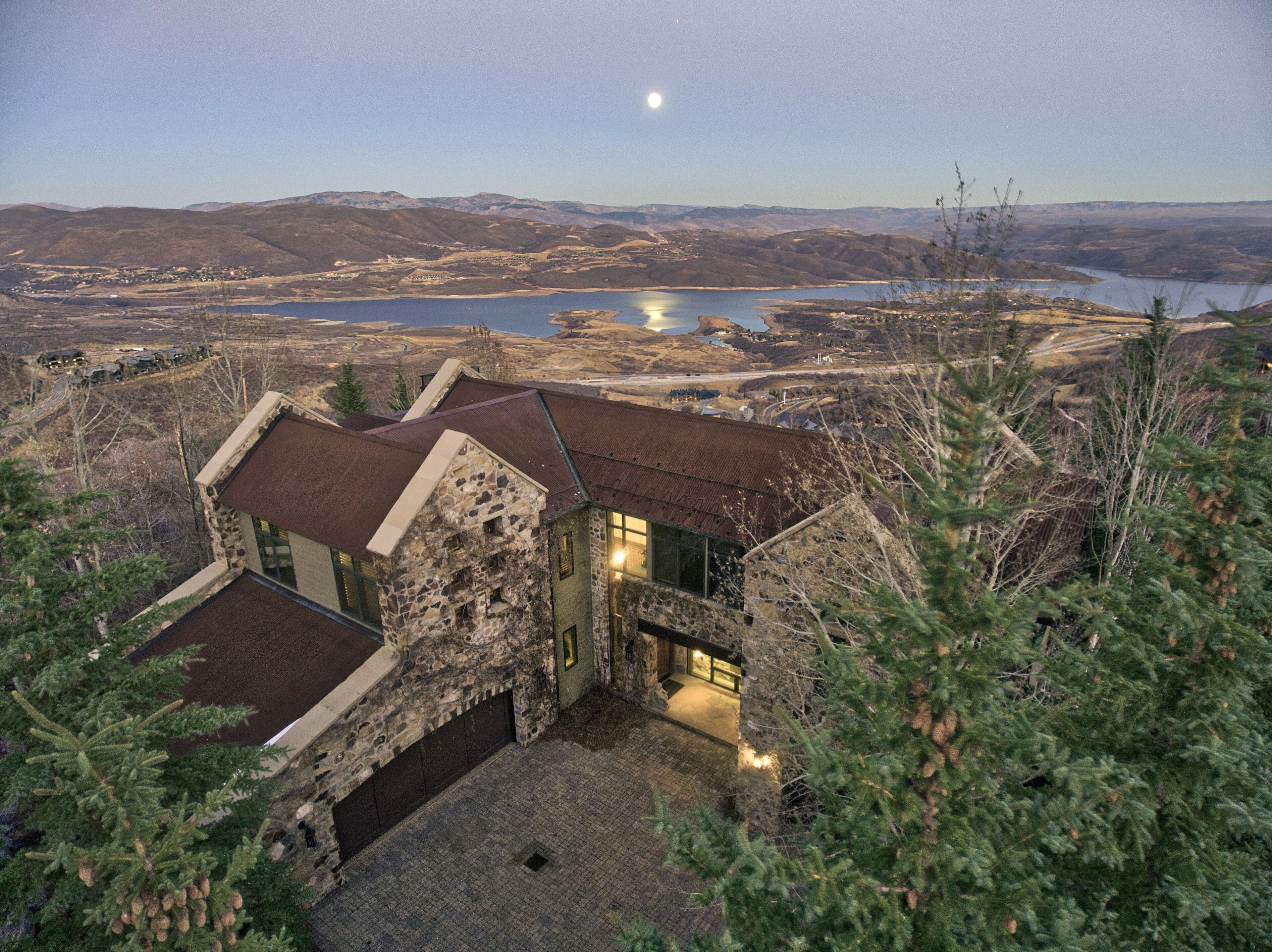 A stone house with a stone chimney, a small porch, and a view of a lake and mountains.