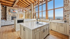 Una cocina amplia con una isla grande, paredes de piedra, vigas de madera y vistas a las montañas.