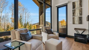 A modern living room with large windows, a glass coffee table, and a fireplace. - Ski-in/ski-out luxury chalet with hot tub, pool, located in The Colony (Park City)