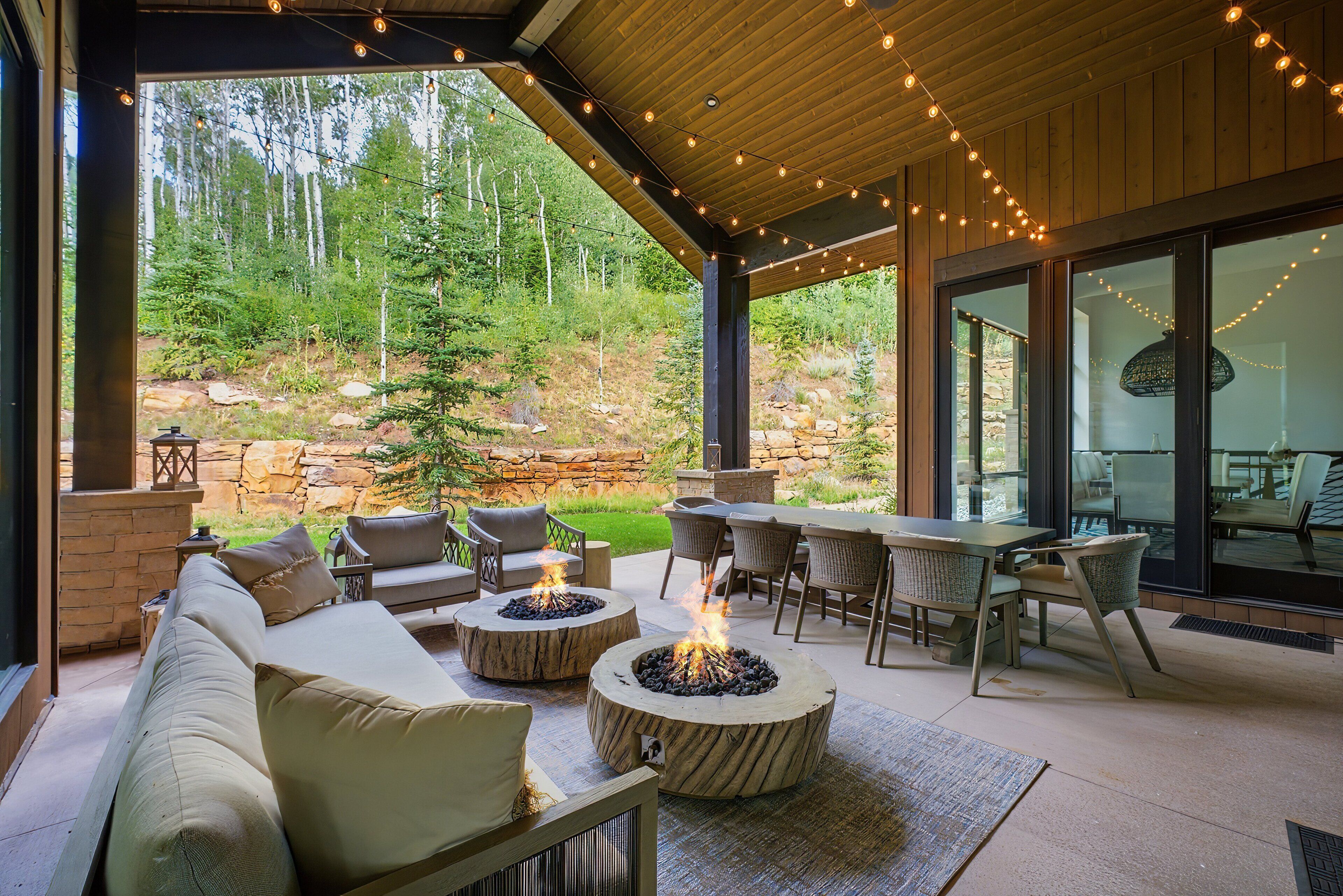 An outdoor patio area with a fire pit, seating, and a view of a forested hillside.