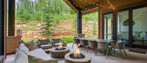 An outdoor patio area with a fire pit, seating, and a view of a forested hillside.