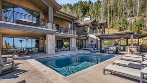 A modern multi-story house with a swimming pool, outdoor seating, and a view of the forest. - Ski-in/ski-out luxury chalet with hot tub, pool, located in The Colony (Park City)