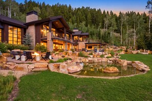 A modern two-story house with a stone facade, a large deck, and a pond. - Ski-in/ski-out luxury chalet with hot tub, pool, located in The Colony (Park City)