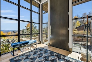 A modern room with large windows, a bench, and a view of the outdoors. - Ski-in/ski-out luxury chalet with hot tub, pool, located in The Colony (Park City)