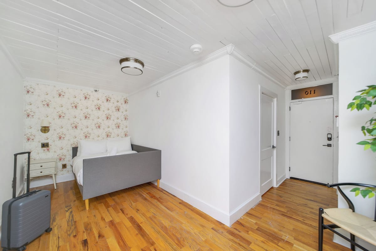 A room with a bed, a suitcase, a small table, a chair, and a door with a sign.