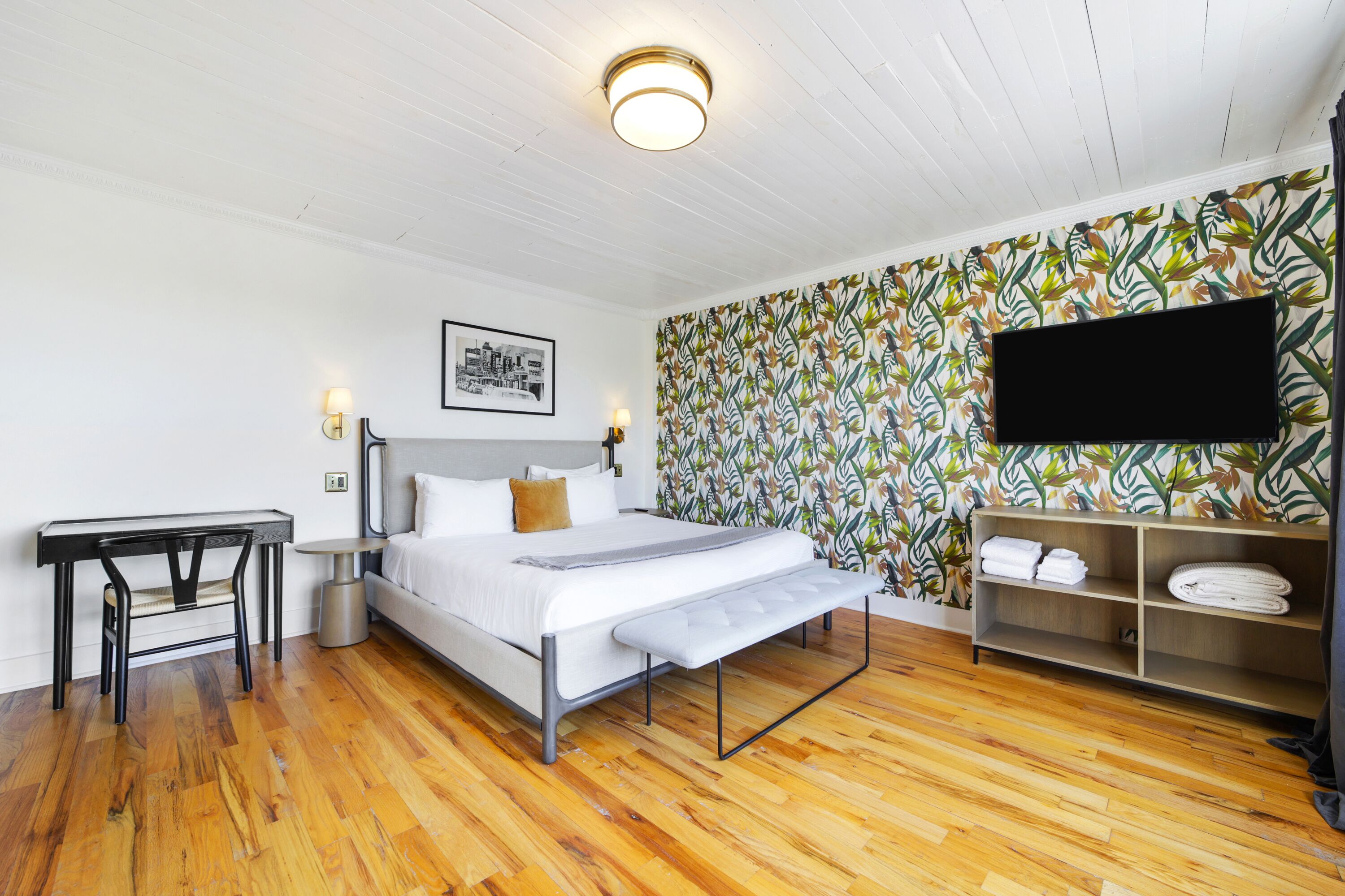A bedroom with a bed, a desk, a TV, and a shelf with towels.
