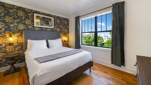 Camera da letto con un letto, un comodino, una lampada a parete, una finestra con tende e vista su del verde all'esterno.