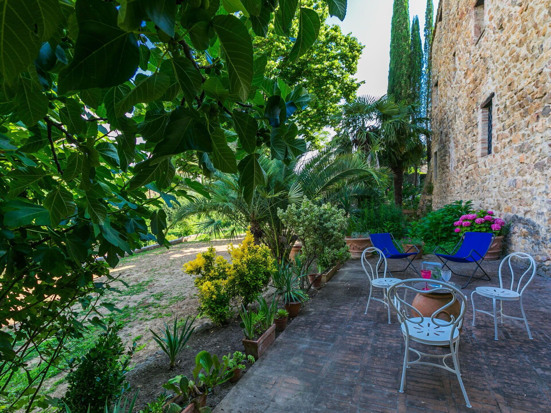 A patio area with outdoor seating, surrounded by lush greenery and a stone building.