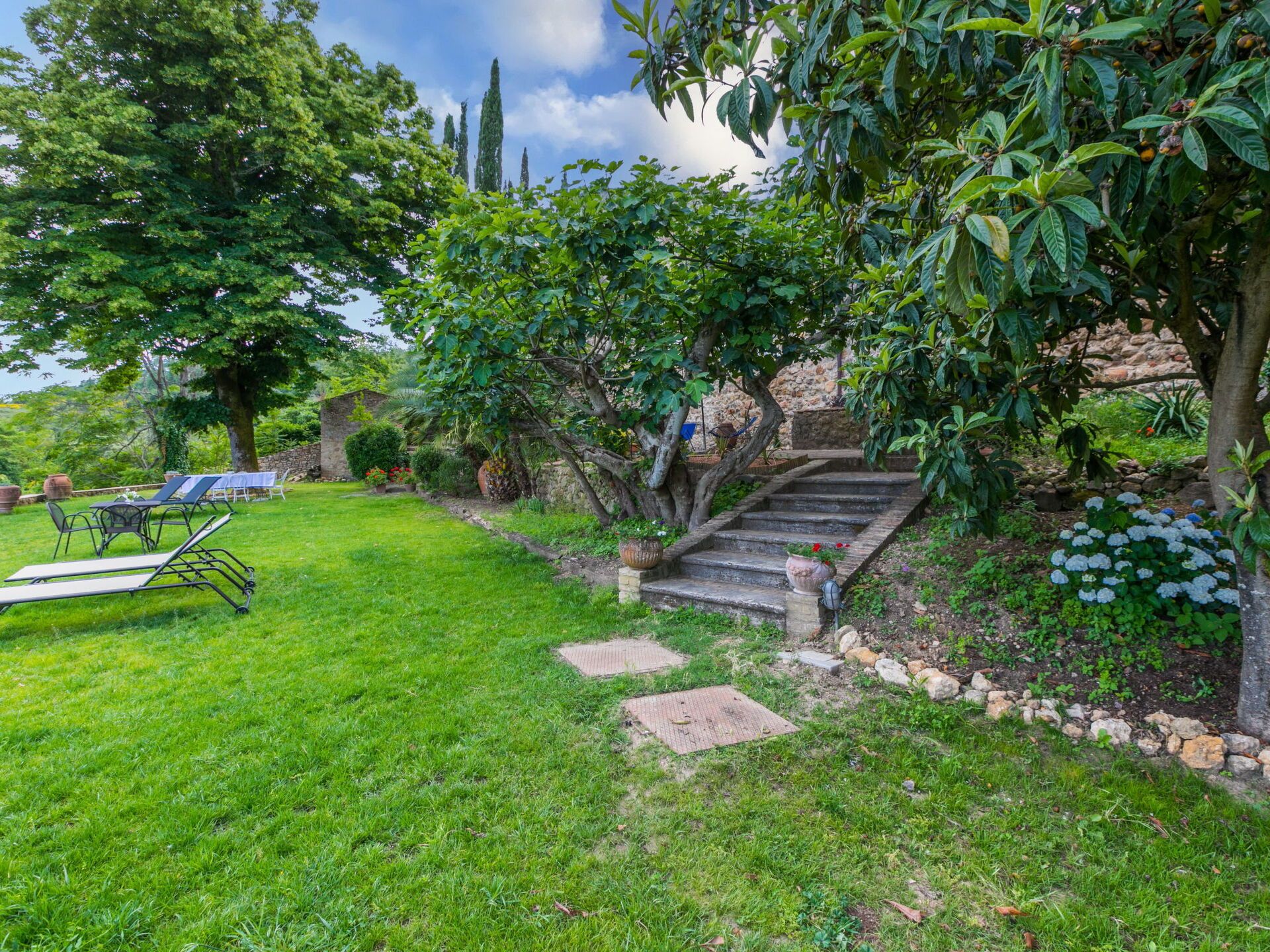 A garden with a stone staircase, a grassy lawn, and a seating area with chairs and a table.