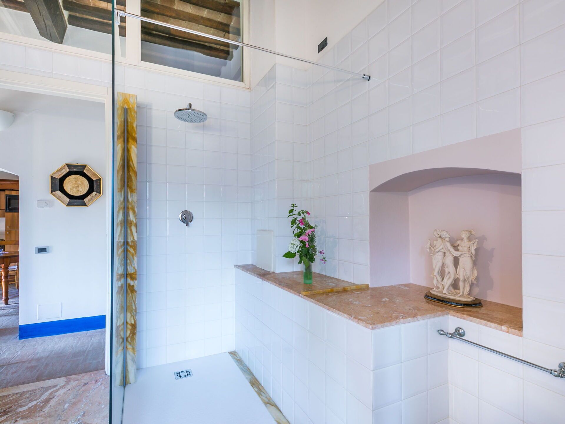 A modern bathroom with white tiles, a glass shower enclosure, a marble countertop, and a decorative statue.