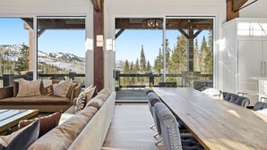 A modern interior with a wooden dining table, cushioned seating, and large windows offering a mountain view. - Luxury & Modern Mountain Chalet in The Colony (Park City)