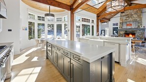 A spacious kitchen with a large island, wooden beams, and a stone fireplace. - Luxury & Modern Mountain Chalet in The Colony (Park City)