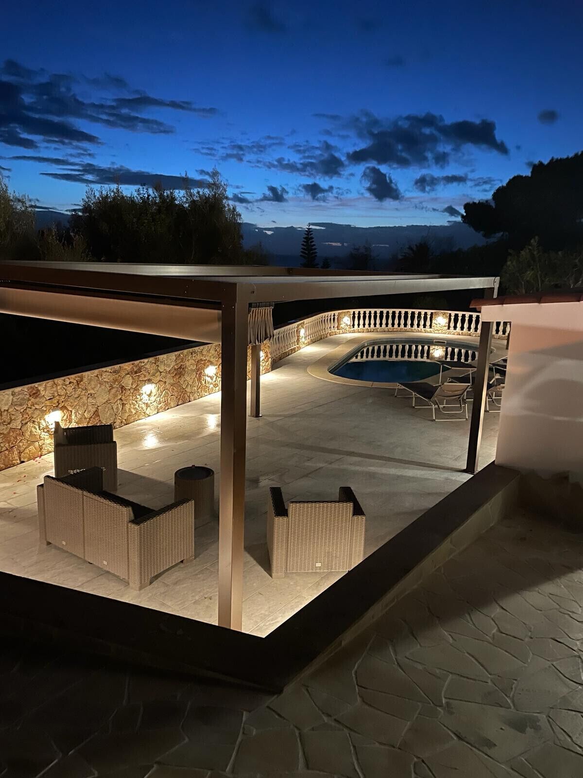 An outdoor patio area with a pool, stone flooring, and wicker furniture.