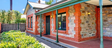 A brick building with a covered porch, stone walls, and a window with a black metal gate.