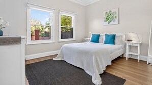 A bedroom with a bed, two windows, a nightstand, a lamp, and a wall art piece.